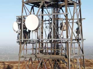 Metal communication tower with several round microwave dishes and aerials, situated outdoors with a hazy landscape in the background—often inspected using non-destructive testing (NDT) methods to ensure structural integrity.